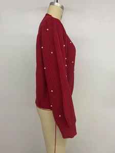 Detail view of red knit sweater featuring delicate white pearl embellishments on sleeves