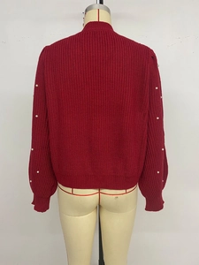 Detail of red cable knit cardigan featuring elegant pearl embellishments on sleeves