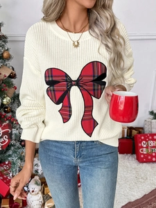 Close-up of white chunky knit sweater featuring a red and black tartan plaid bow detail