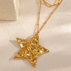 Close-up of golden double-layer necklace with hammered star pendant on stone surface