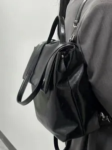 Detail of black glossy leather backpack with silver metal buckles and top handle view