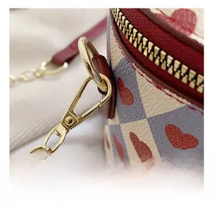 Detail shot of golden metal hooks and red leather trim on a checkered bucket bag
