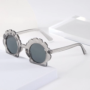 Detail view of translucent grey shell-shaped kids sunglasses with silver glitter accents