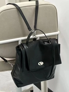 Close-up of black glossy leather backpack with silver oval swivel lock and handle