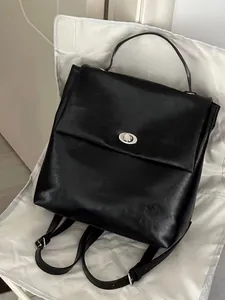 Detail view of the silver metal twist lock closure on the black leather backpack