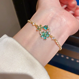 Detail view of 18k gold plated flower bracelet with emerald green stones on female wrist
