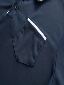 Detail of navy blue piqué polo shirt showing chest pocket with white contrast piping