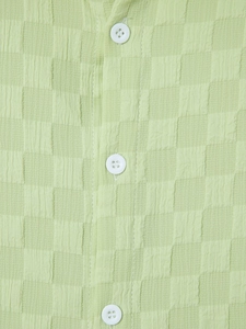 Close-up of avocado green seersucker fabric showing textured checkered pattern and buttons