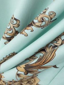 Makro-Detail von minzgrünem Stoff mit goldenen Barock-Blumenprints und Satin-Textur