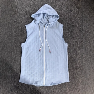 Detail of light blue sleeveless hoodie featuring textured square patterns and white zipper