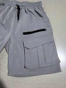 Detail view of grey cargo shorts featuring an elastic drawstring waist and zippered pocket