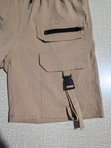 Macro detail of khaki cargo shorts showing side pockets with zippers and buckle straps