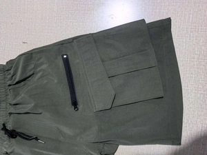 Detail of olive green cargo shorts with elastic waist, drawstring and zipper pocket