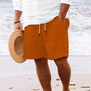 Detail of orange striped beach shorts with drawstring waist against a sandy shore