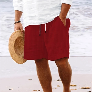 Men's dark red striped beach shorts with white drawstring waist on a sunny beach