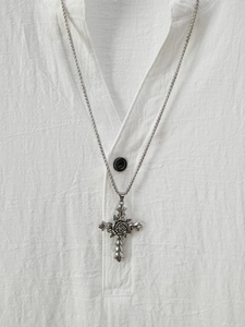 Close-up of a silver rose cross pendant necklace on a white linen shirt background