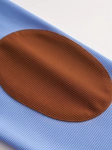 Detailed close-up of brown elbow patches on a blue waffle knit long sleeve polo shirt