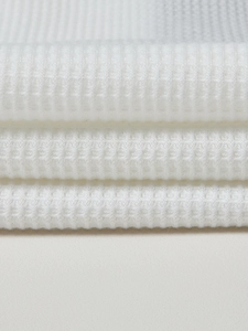 Close-up of premium white waffle knit fabric texture showing the soft 3D honeycomb weave pattern