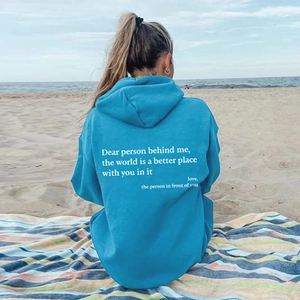 Blue oversized fleece hoodie with white motivational back print on a sunny beach setting