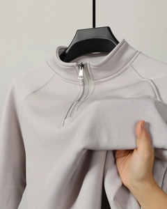 Detail of light grey half-zip polo sweatshirt with fine vertical ribbed texture and metal zipper