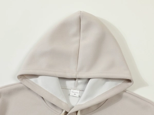 Close-up of beige hoodie collar detail with drawstring and size label inside