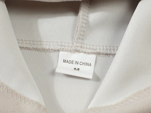 Close-up of the neck label and twill fabric texture on a beige men's hoodie