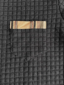 Detail of grey textured polo shirt with plaid trim on the chest pocket and fine stitching
