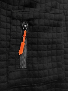 Detailed macro view of black waffle texture fabric featuring a bold orange zipper pull