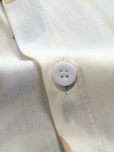 Macro detail of men's floral shirt showing white button and abstract print texture