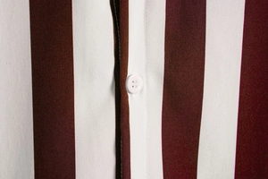 Detail view of burgundy and white vertical stripes on a men's shirt with white button