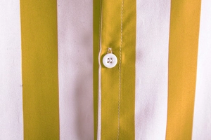 Close-up of yellow and white striped cotton fabric with white resin button and fine stitching