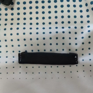 Detail of white mesh fabric with blue dots and black woven strap on men's polo shirt