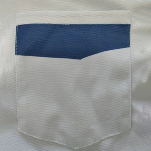 Close-up of chest pocket with navy blue patchwork detail on white polo shirt fabric