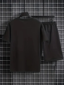 Set sportivo nero da uomo con t-shirt e pantaloncini su parete a griglia metallica