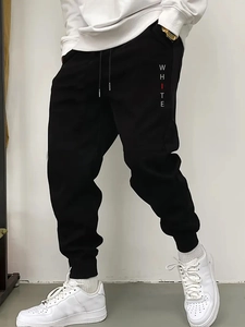 Detail of men's black joggers featuring white letter printing and drawstring waist