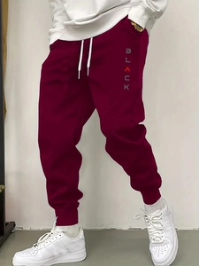 Detail of burgundy joggers showing vertical BLACK letter print and ribbed ankle cuffs