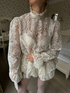 Close-up of white lace high collar top with detailed paisley patterns and ruffles