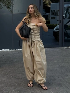 Dettaglio dei pantaloni a lanterna beige da donna con top a fascia e borsa intrecciata