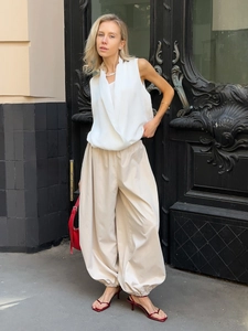 Dettaglio di pantaloni harem beige con polsini elastici e una borsa rossa