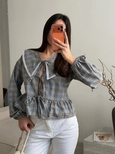 Detailed close-up of a plaid blouse featuring lace trim collar and front bow tie closures