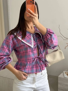Detail of the oversized pointed collar with lace trim and bow-tie closures on plaid shirt