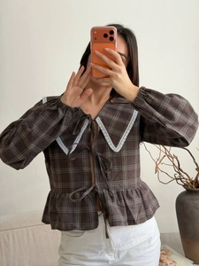 Detail of brown plaid shirt featuring lace collar, bow ties, and puffed lantern sleeves