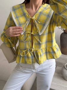 Detailed view of the yellow plaid blouse showing delicate lace trim and bow tie closures