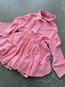 Détail à plat d'une robe rose à manches longues en tissu gaufré avec ourlet à volants