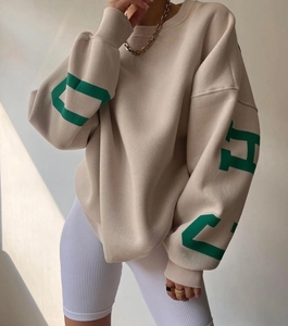 Detail of oversized beige sweatshirt showing dark green letter prints and ribbed cuffs