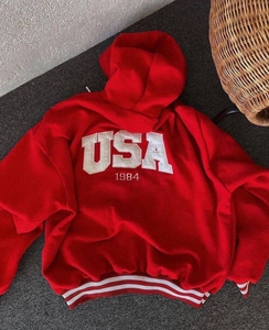 Detail of red hoodie featuring white USA 1984 embroidery and striped ribbed cuffs