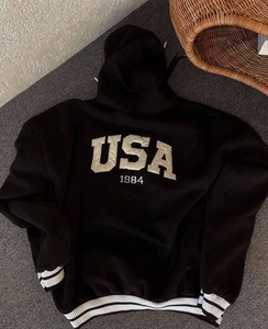 Close-up of black oversized hoodie featuring white USA 1984 print and striped ribbed cuffs