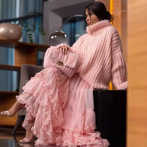 Pink oversized turtleneck knit sweater and layered ruffle skirt with plush envelope clutch