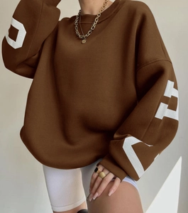 Close-up of brown oversized sweatshirt featuring white letter prints on sleeves and ribbed cuffs