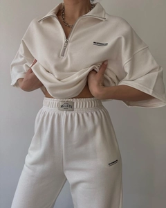 Detail of cream track suit showing half-zip sweatshirt collar and MAI STUDIOS CO logo print